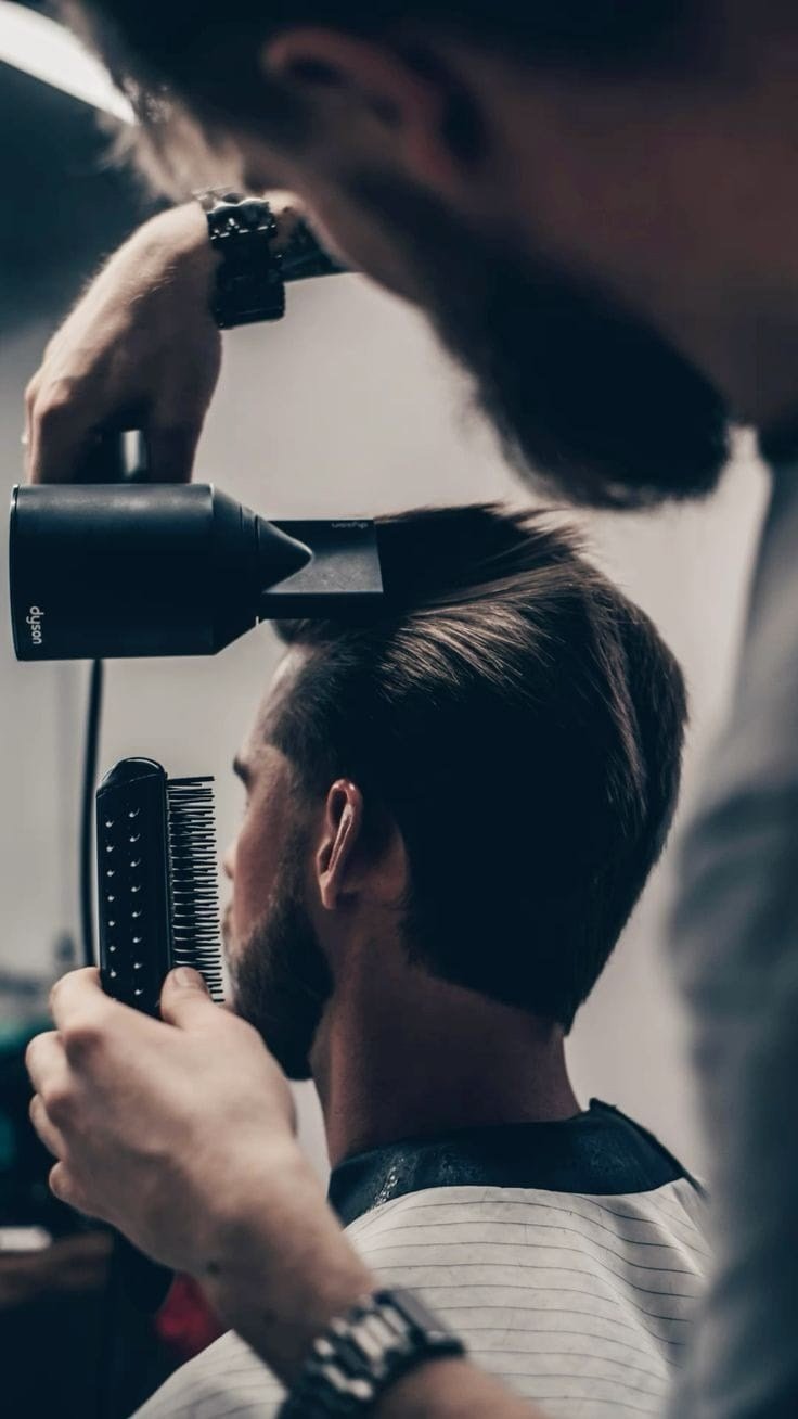 Een barbier brengt het haar zorgvuldig in model met borstel en föhn